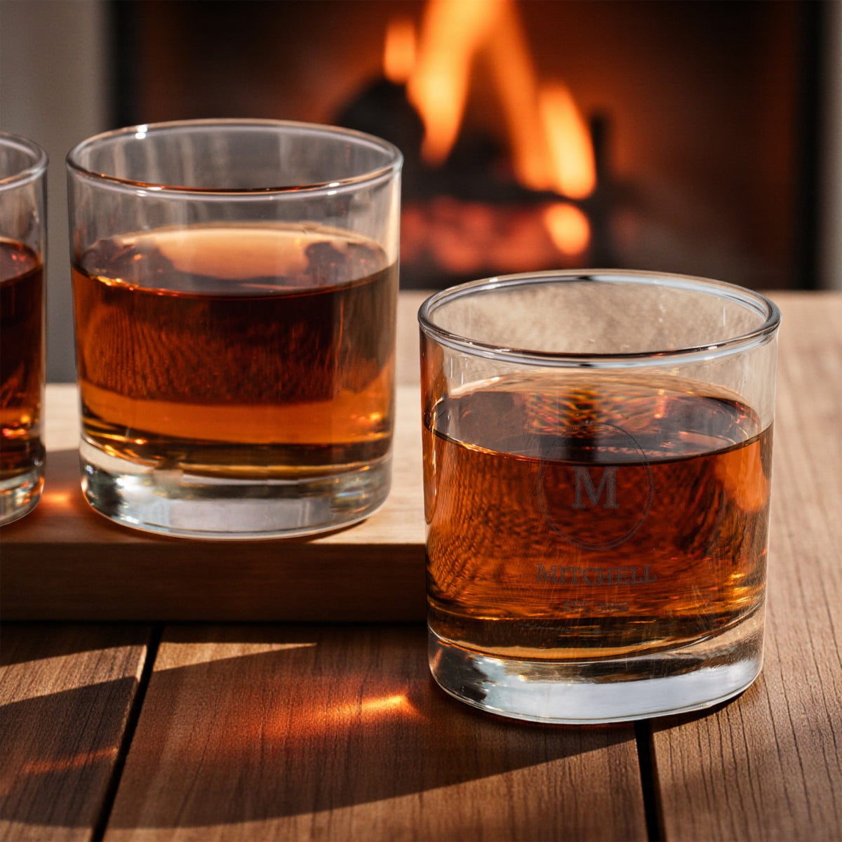 Two etched monogram whiskey glasses by a fireplace