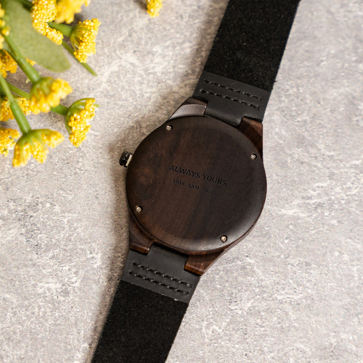 Back of a dark wood watch with a black strap, laser-engraved with a two-line personal message