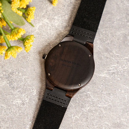Back of a dark wood watch with a black strap, laser-engraved with a two-line personal message