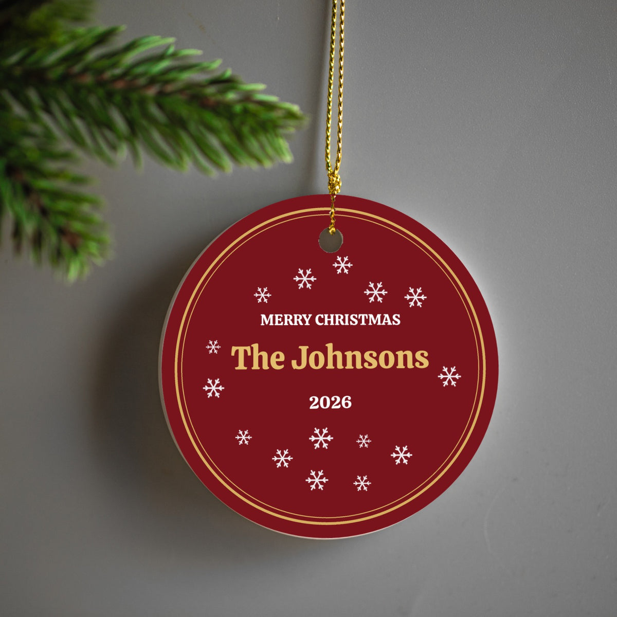 Red snowflake ceramic ornament personalized with The Johnsons 2026 hanging by a pine branch
