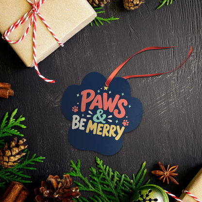 Paws & Be Merry paw print ornament on a dark table with pine branches, pinecones and a wrapped gift