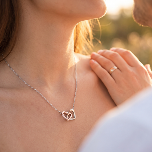 Woman wearing the rose gold and silver interlocking hearts necklace, partner's hand on her shoulder at golden hour