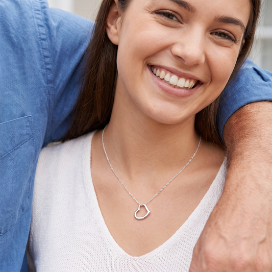 Smiling daughter wearing a delicate silver open-heart necklace, her dad's arm around her shoulder