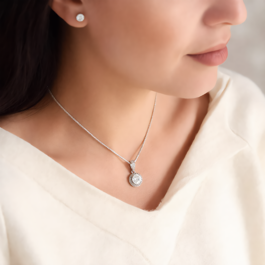Woman wearing the silver Eternal Hope necklace, a round clear cubic zirconia halo pendant on a fine chain, with matching CZ stud earring, in a cream sweater
