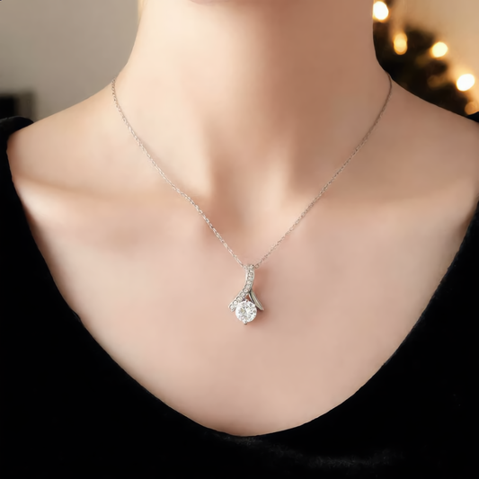 Woman wearing the silver Alluring Beauty ribbon pendant with a round clear cubic zirconia stone on a fine chain, black velvet top, holiday lights behind